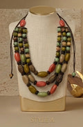 A multi-strand statement necklace displayed on a cream fabric mannequin bust. The necklace features a mix of olive green, terracotta red, brown, and beige beads with dark brown cord ties.