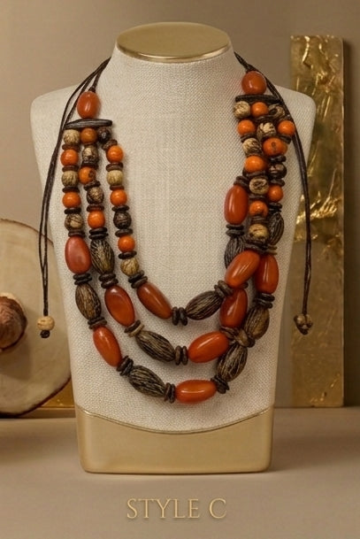 A multi-strand statement necklace displayed on a cream fabric-covered jewelry bust. The necklace features alternating large orange-brown polished beads and dark brown wood beads on black cords.