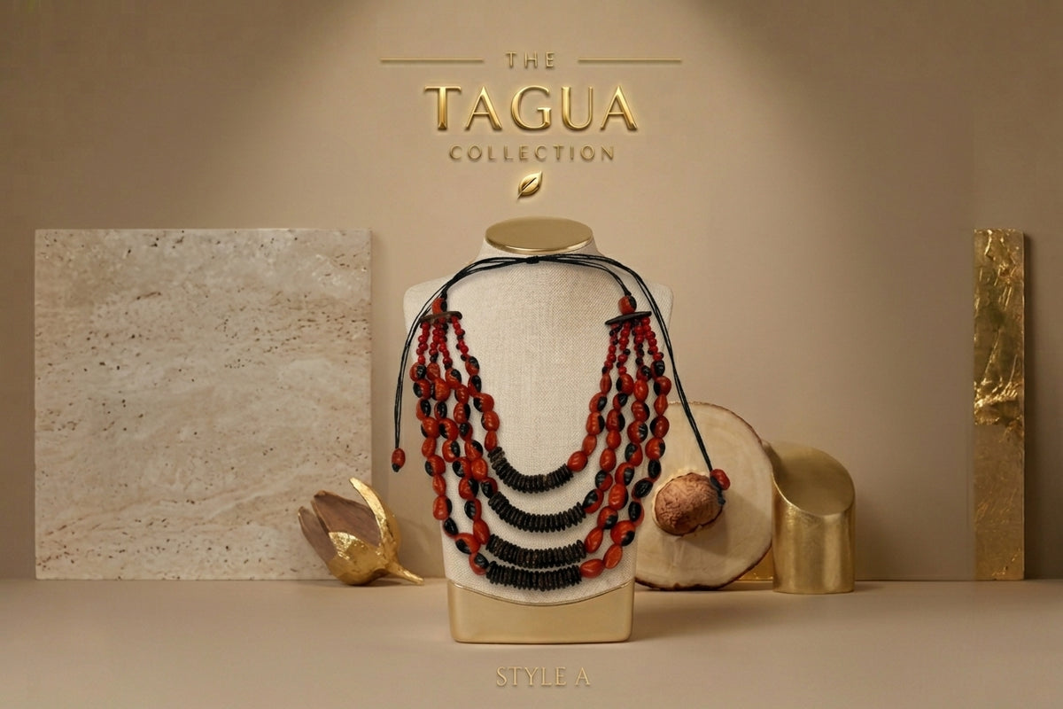 A multi-strand beaded necklace displayed on a cream fabric mannequin bust, featuring red and black beads with a dark cord. The bust is styled with gold props and stone slabs against a beige background with 'THE TAGUA COLLECTION' text at the top.