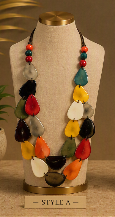 A multi-strand statement necklace with colorful teardrop-shaped beads displayed on a beige fabric mannequin bust. The necklace features beads in red, orange, yellow, green, black, and white, with a dark cord and red/green bead accents at the top.