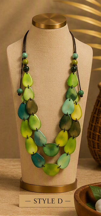 A multi-strand statement necklace displayed on a beige fabric jewelry bust. The necklace features layered rows of glossy, teardrop-shaped beads in shades of lime green, forest green, and teal blue, accented with small green and dark beads on a black cord.