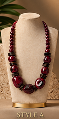 A long statement necklace displayed on a beige fabric jewelry bust. The necklace features alternating large and small glossy dark red beads with black spacer rings, with a large oval bead at the center.
