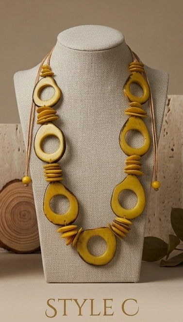 A yellow beaded necklace with large circular and oval beads, displayed on a beige fabric jewelry bust. The necklace includes small yellow spacer beads and cord details.