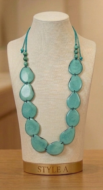 A turquoise beaded necklace displayed on a cream fabric mannequin bust with a gold base labeled 'STYLE A', set against a warm beige background.