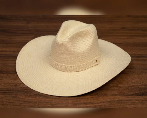 A light beige woven straw cowboy hat with a wide brim and a matching band, resting on a dark brown wooden surface. Ecuadorian Toquilla Straw Hat.