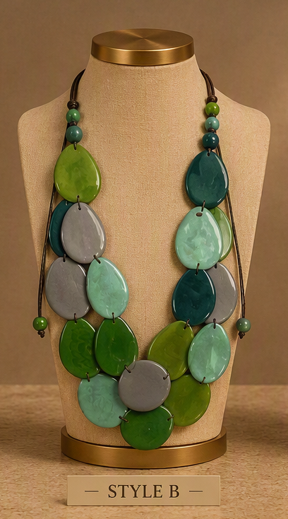 A multi-strand statement necklace displayed on a beige fabric mannequin bust with a gold-colored top and base. The necklace features multiple strands of teardrop-shaped beads in shades of green, teal, and gray, suspended from dark cords with small green bead accents.
