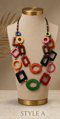 A multicolor statement necklace with geometric tagua links displayed on a beige fabric mannequin bust with gold-toned top and bottom. The necklace features black, red, orange, green, pink, and brown links, Ecuadorian tagua necklace