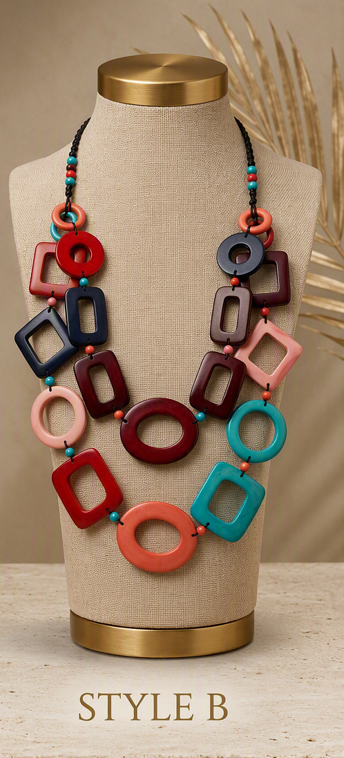 A double-strand statement necklace displayed on a beige fabric mannequin bust with gold-toned top and bottom caps. The necklace features large, colorful geometric links in coral, red, teal, pink, navy, and purple, separated by small turquoise beads,, Ecuadorian tagua necklace.