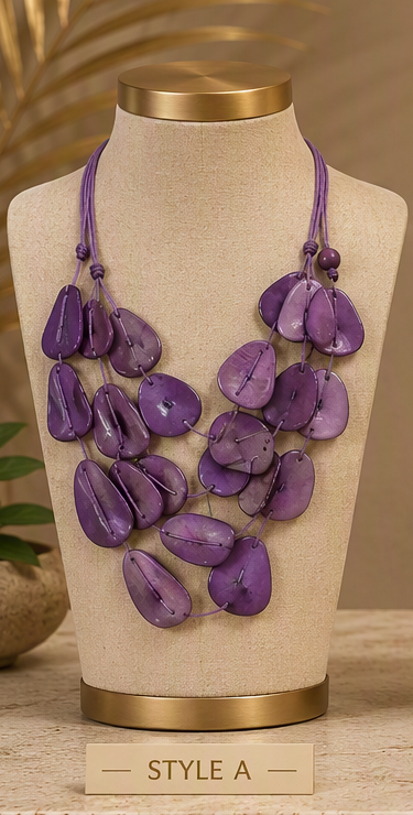 A purple shell-bead statement necklace displayed on a beige fabric jewelry bust with gold-tone trim. The necklace features multiple strands of teardrop-shaped purple shells on cord.