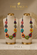 Two beige jewelry display busts wearing matching colorful statement necklaces from The Tagua Collection, shown against a warm beige background with decorative palm leaves and the text 'THE TAGUA COLLECTION' and 'STYLE A'.
The Tagua Classic Beaded Necklace in Style A, Ecuadorian tagua necklace.