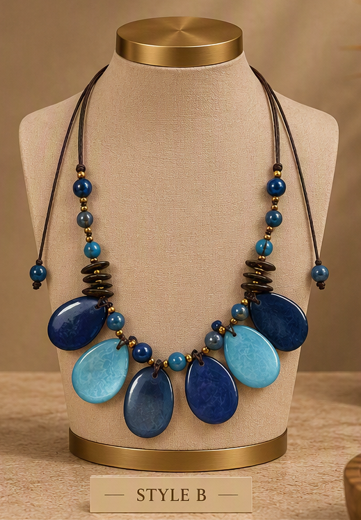 A multi-strand statement necklace displayed on a beige fabric jewelry bust. The necklace features dark brown cords, small blue and turquoise beads, and large teardrop-shaped beads in navy blue and light turquoise.