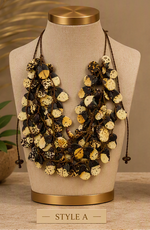 A multi-strand statement necklace displayed on a beige fabric mannequin bust with gold-toned caps. The necklace features layered dark brown cords adorned with round, textured shell-like beads in cream, black, and brown mottled patterns.
