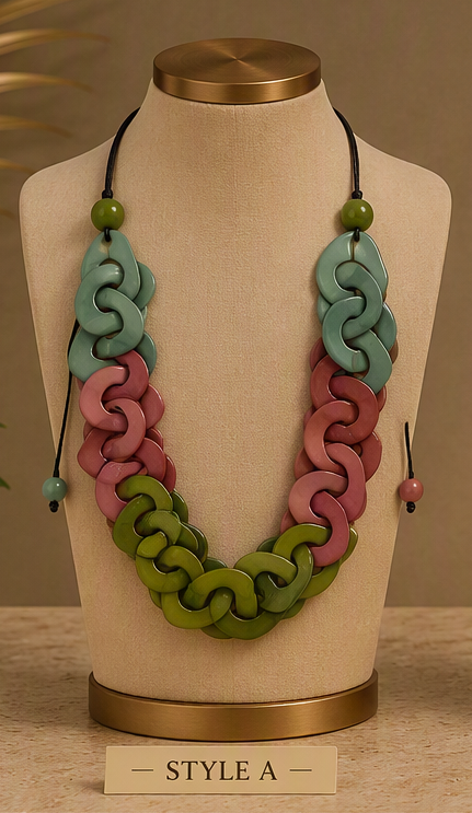 A multi-strand wooden link necklace displayed on a beige fabric jewelry bust. The necklace features three distinct strands of interlocking wooden links in sage green, dusty pink, and mint green, accented with small round green beads on black cords, Ecuadorian tagua necklace.