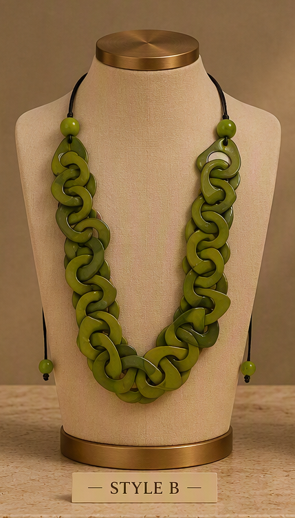 A green chunky interlocking link necklace displayed on a beige fabric jewelry bust with a gold-toned top and base. The necklace has matching green beads and black cords, Ecuadorian tagua necklace.