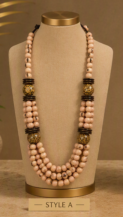 A multi-strand beaded necklace displayed on a beige jewelry bust. The necklace features multiple strands of light pinkish-beige beads, accented with dark brown textured spacer beads and two large round gold-toned beads with black detailing.