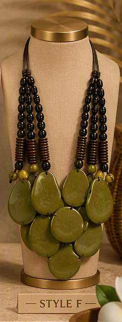 A statement necklace displayed on a beige jewelry bust. The necklace features large olive green stone-like teardrop pendants at the bottom, with multiple strands of dark brown and black beads and small green accent beads above.